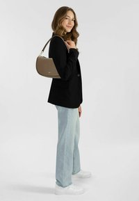 Blazer nero su jeans a gamba larga blu chiaro, abbinato a una borsa curva marrone e sneakers bianche con platform. Texture morbide in tutto l'outfit.