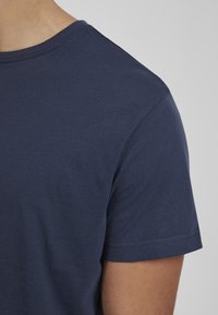 Mornarska majica s kratkim rukavima i okruglim izrezom, izrađena od glatkog pamučnog materijala, sadrži suptilnu teksturu i šivene detalje na rukavima i rubovima.