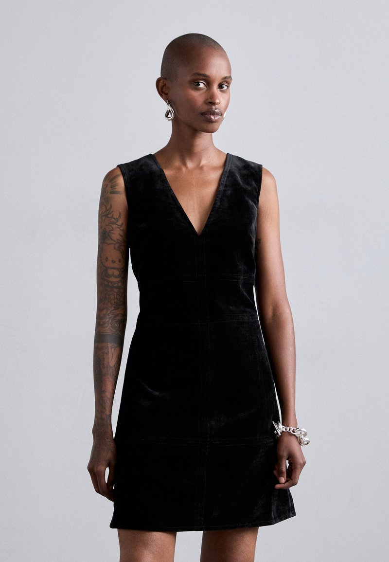 Rochie din catifea neagră, fără mâneci, cu decolteu în V, corset ajustat și fustă evazată. Prezintă cusături minimaliste și o textură netedă.