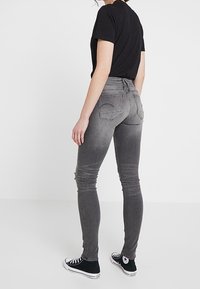 Grå smala jeans med en blekt tvätt, knapp- och dragkedjestängning, bakfickor; tillsammans med en svart t-shirt och svarta sneakers.