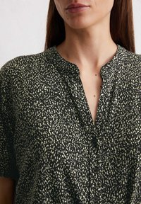 Zwarte shirt met een groen gespikkeld patroon, voorzien van een ronde halslijn, knoopsluiting en een lichtgewicht stof met een soepele textuur.