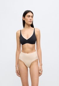 Μαύρο μπουστάκι με γυμνή απόχρωση γύρω από το λαιμόκομμα, συνδυασμένο με σλιπ ψηλόμεσο σε γυμνή απόχρωση. Λεία υφή, μινιμαλιστικός σχεδιασμός.