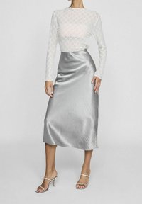 Top à manches longues en dentelle blanche avec une jupe midi en satin argenté. La jupe est lisse avec un léger éclat, assortie à des sandales à talons argentées.