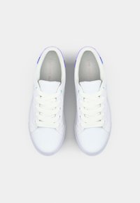 Baskets blanches avec une tige en cuir lisse, présentant des accents bleu clair sur les œillets et une languette de talon violette. Design classique à lacets.