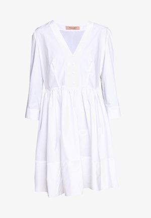 Biała sukienka z dekoltem w kształcie litery V, rękawami o długości trzech ćwierć, zapinana na guziki z przodu i zebranym w pasie. Posiada rozkloszowany krój i gładką bawełnianą teksturę.