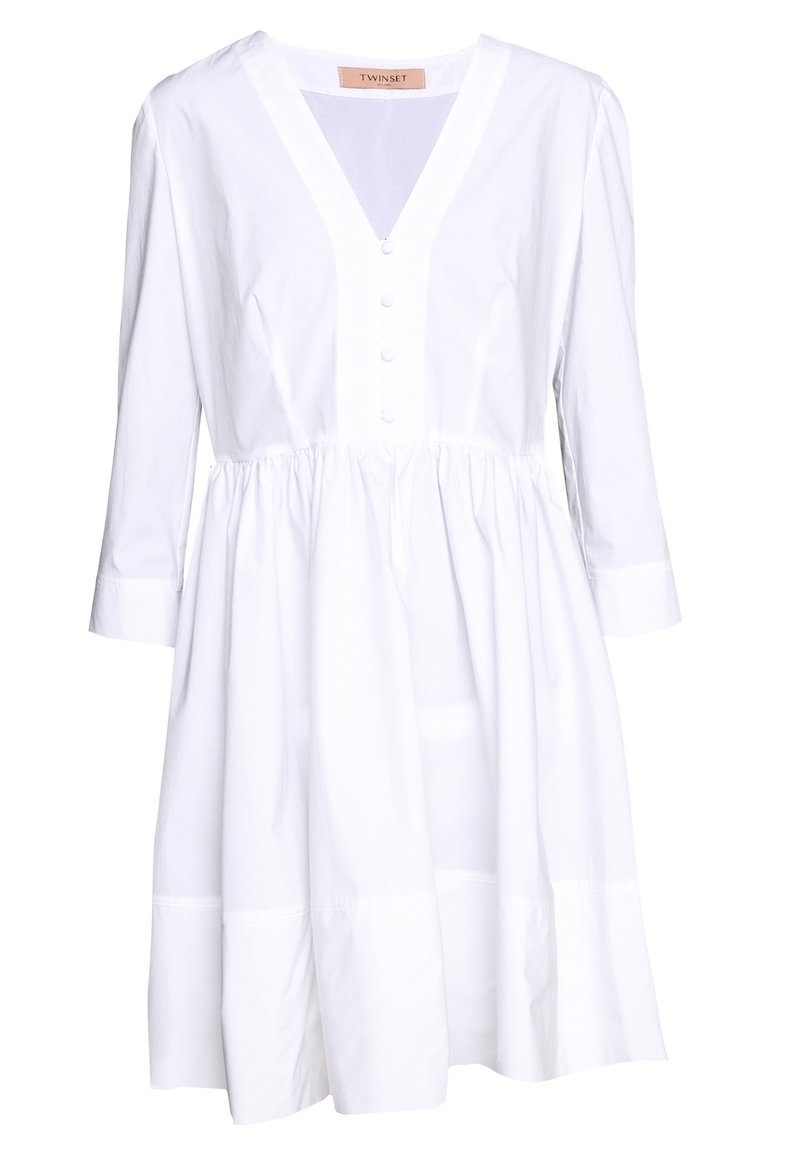 Vestido blanco con escote en V, mangas tres cuartos, cierre de botones en la parte delantera y cintura fruncida. Presenta una silueta acampanada y una textura de algodón suave.