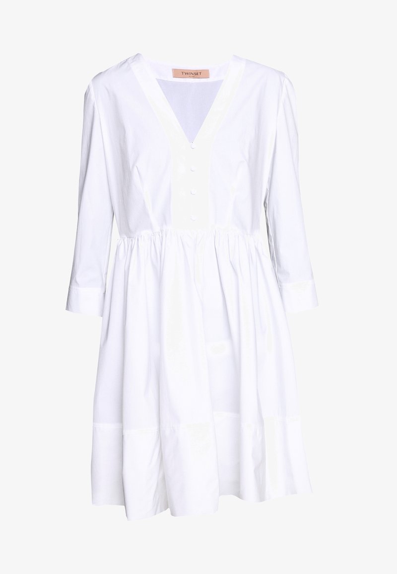 Vestido blanco con escote en V, mangas tres cuartos, cierre de botones en la parte delantera y cintura fruncida. Presenta una silueta acampanada y una textura de algodón suave.