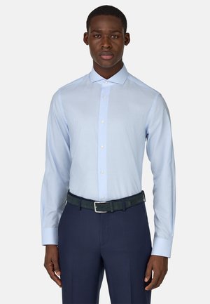 Camisetta azzurro chiaro con un sottile motivo a righe, colletto button-down e maniche lunghe. Abbinata a pantaloni blu scuro e una cintura verde.