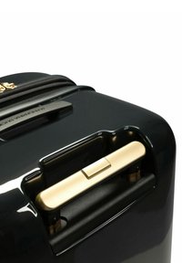 Schwarzer Hartschalenkoffer mit glänzender Oberfläche, goldenen Beschlägen und einem strukturierten Griff. Auffälliger Ziehmechanismus und sichtbares Markenlabel.