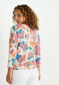 Pull en tissu doux à motif floral multicolore ; présente un col bateau et des manches trois-quarts ; accents principalement roses, bleus et verts.