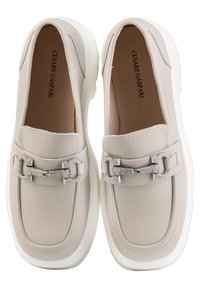 Mocassins en cuir beige avec un détail de chaîne argentée brillante, semelle en caoutchouc blanche, bout rond et accents cousus sur le dessus. Design plat.