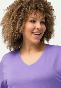 Lila V-Ausschnitt T-Shirt aus weichem Stoff, mit glatter Textur und kurzen Ärmeln. Nahaufnahme des Ausschnitts und des Schulterbereichs.