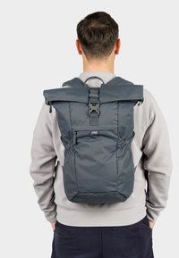 Grau rolltop Rucksack mit verstellbaren Trägern, strukturiertem Stoff, vorderer Schnallenverschluss und Seitentaschen. Robuste Bauweise und kompakte Form.