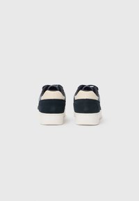Baskets en daim et cuir bleu marine avec une semelle en caoutchouc blanc, présentant une texture lisse et un design minimaliste. Vue arrière montrant une couleur bicolore.