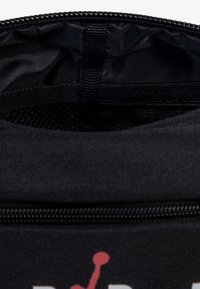 Sac isolant noir avec fermeture éclair et poche en maillage intérieur. Présente une surface texturée et un logo graphique de couleur contrastante.