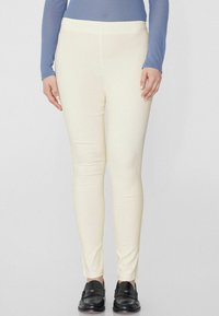 Leggings de couleur crème avec une texture lisse et extensible. Design taille haute. Associés à des chaussures noires à enfiler.