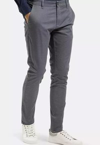 Lekki, szary materiał spodni o teksturowanym wzorze, slim fit, z bocznymi kieszeniami, w połączeniu z białymi trampkami z czerwonymi i szarymi akcentami.