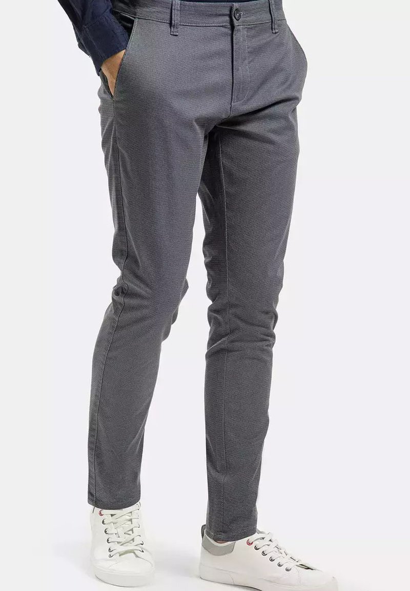 Lekki, szary materiał spodni o teksturowanym wzorze, slim fit, z bocznymi kieszeniami, w połączeniu z białymi trampkami z czerwonymi i szarymi akcentami.