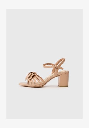 Sandale à talon beige avec une ouverture à l'avant, ornée d'un accent floral sur le bout et d'une sangle autour de la cheville avec une boucle. Talon bloc arrondi.