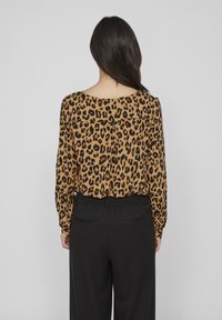 Bluză cu imprimeu leopard în nuanțe de bej și negru, cu mâneci lungi și o croială lejeră, asortată cu pantaloni negri cu talie înaltă. Material texturat, ușor.