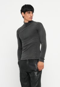 Dugi rukav, tamnosivi rebrasti turtleneck. Ima uski dizajn, teksturiranu tkaninu, asimetričnu izrezanu liniju i minimalne šavove.