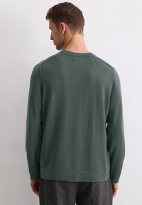Ciemnozielony sweter z dzianiny z długimi rękawami, ściągaczami oraz okrągłym dekoltem. Gładka tekstura i minimalistyczny design bez widocznych wzorów.