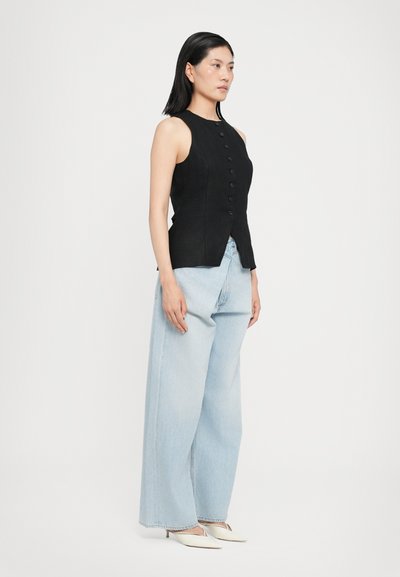 Black sleeveless top featuring a button front, paired with light blue wide-leg jeans. White pointed-toe heels complete the outfit.