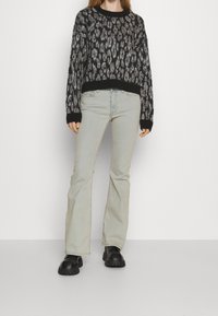 Svart och gråmönstrad stickad tröja med lös passform, parat med ljusblå utsvängda jeans och kraftiga svarta skor.