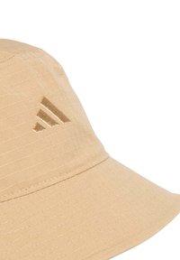 Beige bucket hat with textured fabric, featuring a wide brim and a subtle, embossed three-stripe logo on the side.