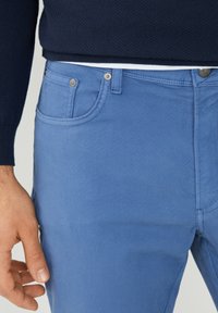 Pantalones de algodón azul claro con diseño de cinco bolsillos, herrajes plateados y corte recto. La tela tiene una textura suave y un aspecto informal.