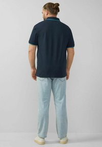 Dunkelblaues Polohemd mit Kragen und grünen Akzenten, kombiniert mit hellblauen Jeans und cremefarbenen Sneakers. Rückansicht.