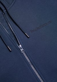 Marineblå zip-hoodie lavet af glat stof. Har en fuld lynlås, flade snore og "Peak Performance"-logo broderet i matchende farve.