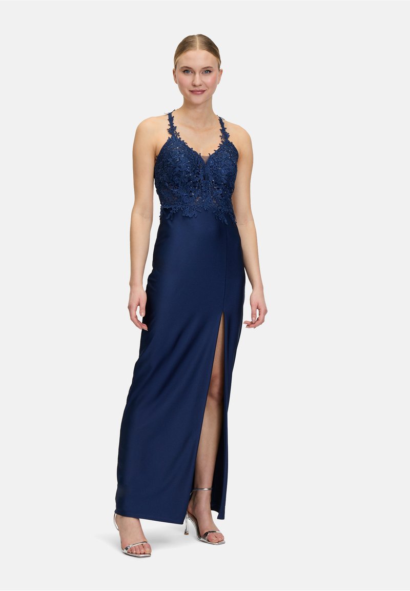 Granatowa suknia z koronkowym topem, regulowanymi ramiączkami i rozcięciem do uda; gładka struktura materiału; noszona z srebrnymi sandałami na obcasie.