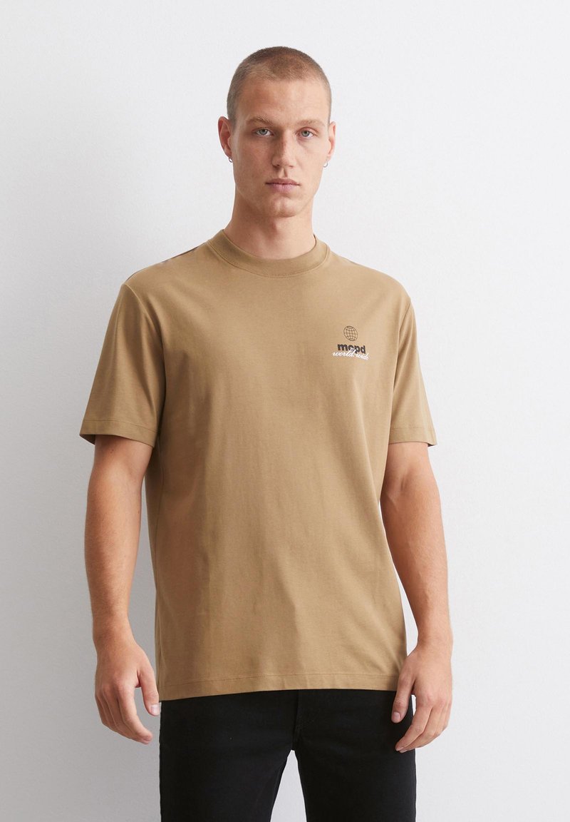 Brun bomull t-skjorte med rund hals, korte ermer og en liten globuslogo på brystet. Stoffet ser glatt og ensfarget ut.