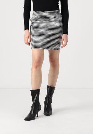 Mini-jupe à motif pied-de-cochons noir et blanc avec un tissu froncé à la taille, associée à des bottes noires à talons hauts jusqu'aux genoux.
