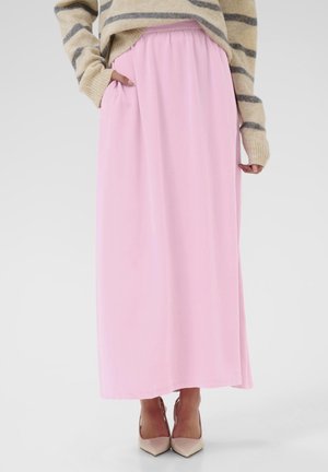 Personne portant une longue jupe rose clair avec des poches, un pull beige à rayures et des escarpins beiges à bout pointu.