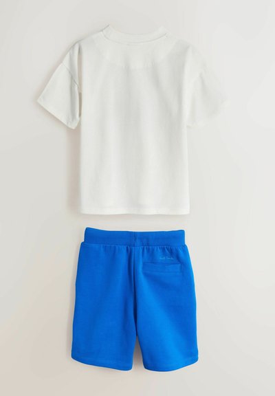 Camiseta blanca de manga corta combinada con pantalones cortos azules de cintura elástica con un bolsillo trasero y un pequeño bordado de logo.