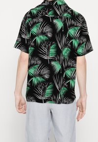 Svart kortärmad skjorta med mönster av gröna och vita palmblad. Lättviktig tyg med avslappnad passform och standard krage.