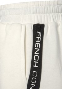 Weiße Jogginghose aus strukturiertem Stoff. Sie hat einen elastischen Bund und einen schwarzen Seitenstreifen mit weißem Text, der "FRENCH CONNECTION" sagt.