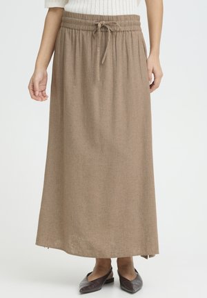 Kvinde iført en beige maxi nederdel med snøre og lommer samt brune flade sko med spidse tæer på en hvid baggrund.