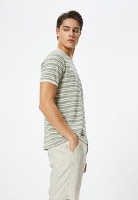 Stripet kortærmet t-shirt i lys creme og oliven med rund hals, parret med lyse afslappede bukser. Glat bomuldsstruktur.