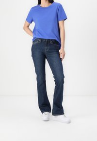 T-shirt en coton bleu à manches courtes, associé à un jean en denim bleu foncé. Des baskets blanches complètent la tenue. Design simple et décontracté.