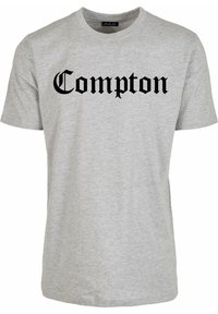 Lichtgrijs T-shirt met korte mouwen en ronde hals, met "Compton" in grote zwarte Old English letters gecentreerd op de voorkant.