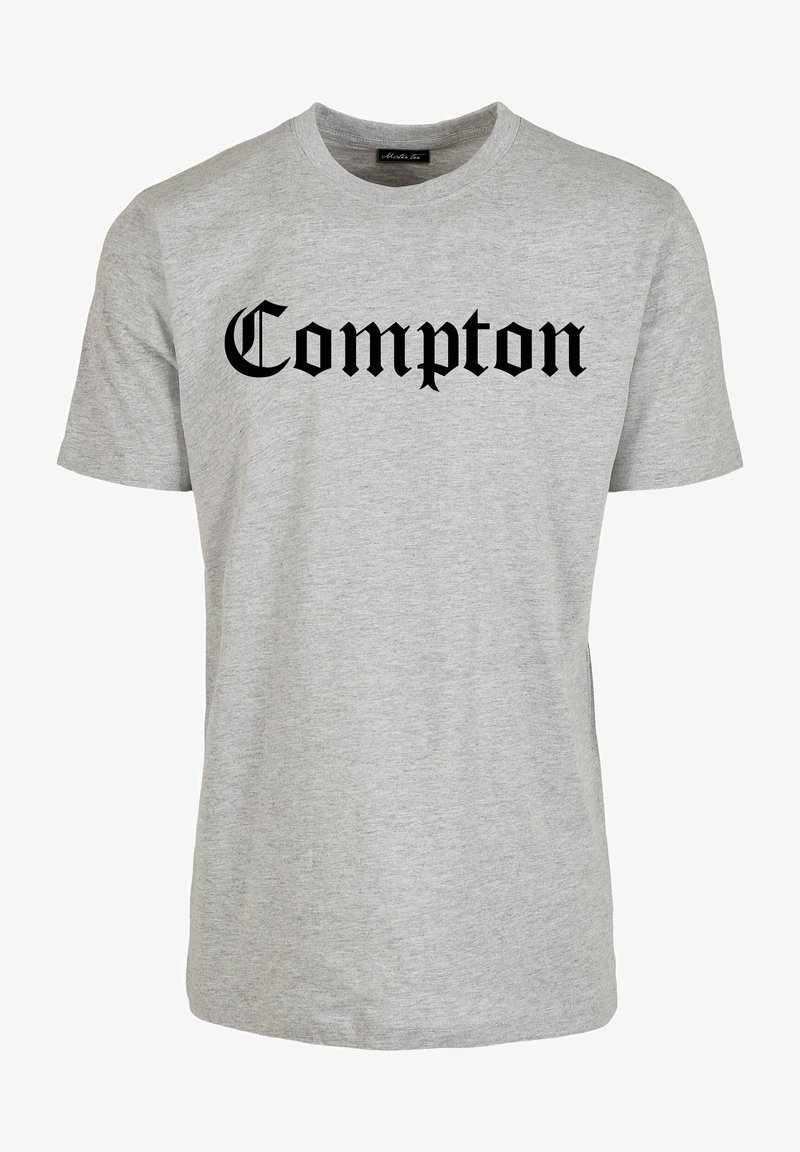 Lichtgrijs T-shirt met korte mouwen en ronde hals, met "Compton" in grote zwarte Old English letters gecentreerd op de voorkant.