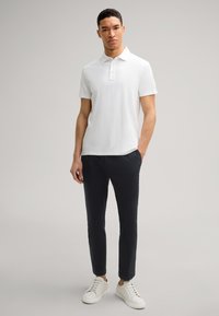 Witte polo met korte mouwen en kraag, gecombineerd met navy slim-fit broek en witte sneakers, met een schoon, minimalistisch ontwerp.