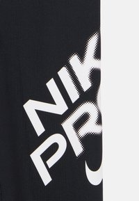 Μαύρο αθλητικό τοπ με μεγάλα λευκά γράμματα που γράφουν "NIKE PRO." Το ύφασμα είναι λείο και εφαρμοστό, με διακριτική υφή με τελείες που τονίζουν τα γράμματα.