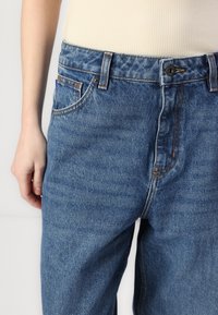 Τζιν παντελόνια σε ανοιχτό μπλε με ελαφρώς ξεθωριασμένη υφή, με ραφές από χαλκό, πέντε τσέπες και κούμπωμα με κουμπί στη μέση.