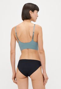 Hellblaues Sport-BH mit verstellbaren Trägern kombiniert mit schwarzen Badehosen, die eine glatte Textur und ein einfaches Design aufweisen.