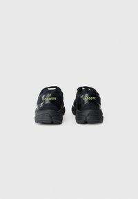 Juodi Lacoste sportbačiai su tinklu ir sintetiniais akcentais, kuriuose yra tekstūruotas padas ir žalias logotipas ant kulno bei liežuvio.