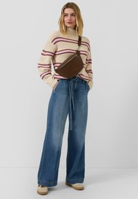 Brązowa torebka na ramię o zakrzywionym kształcie, noszona z kremowym swetrem w różowe paski i szerokimi dżinsami o szerokich nogawkach.